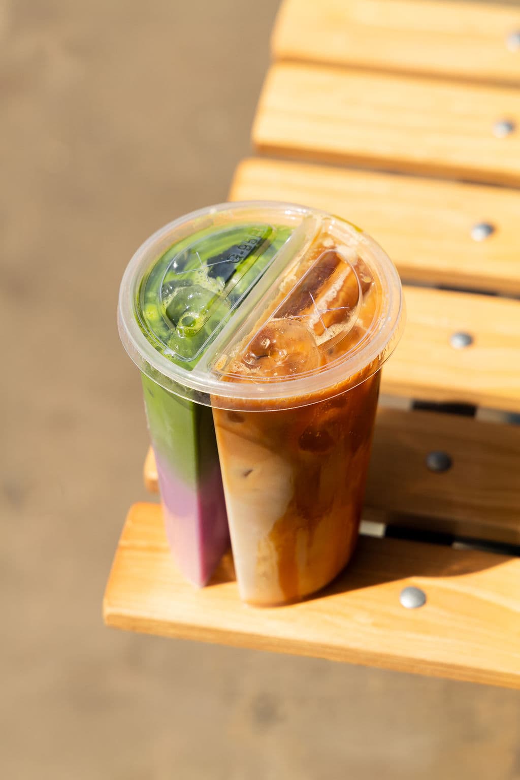 Our split cup with iced matcha and coffee, on a sunny bench